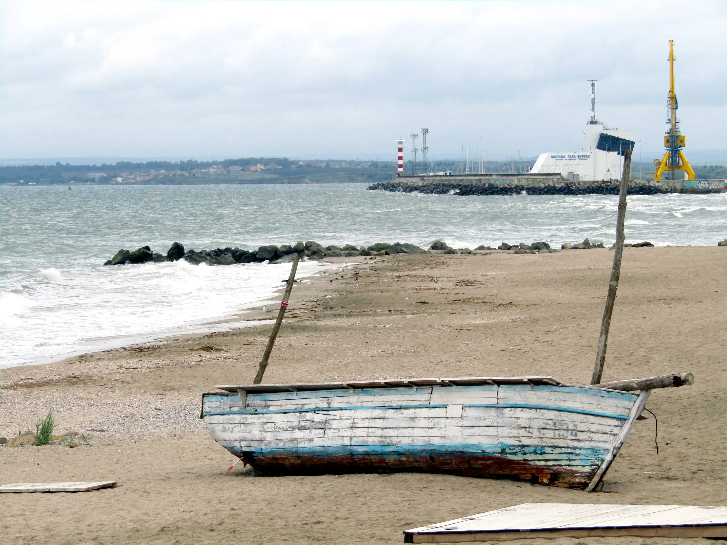 The city beach at Burgas with the port breakwater, a lighthouse and a cargo crane behind