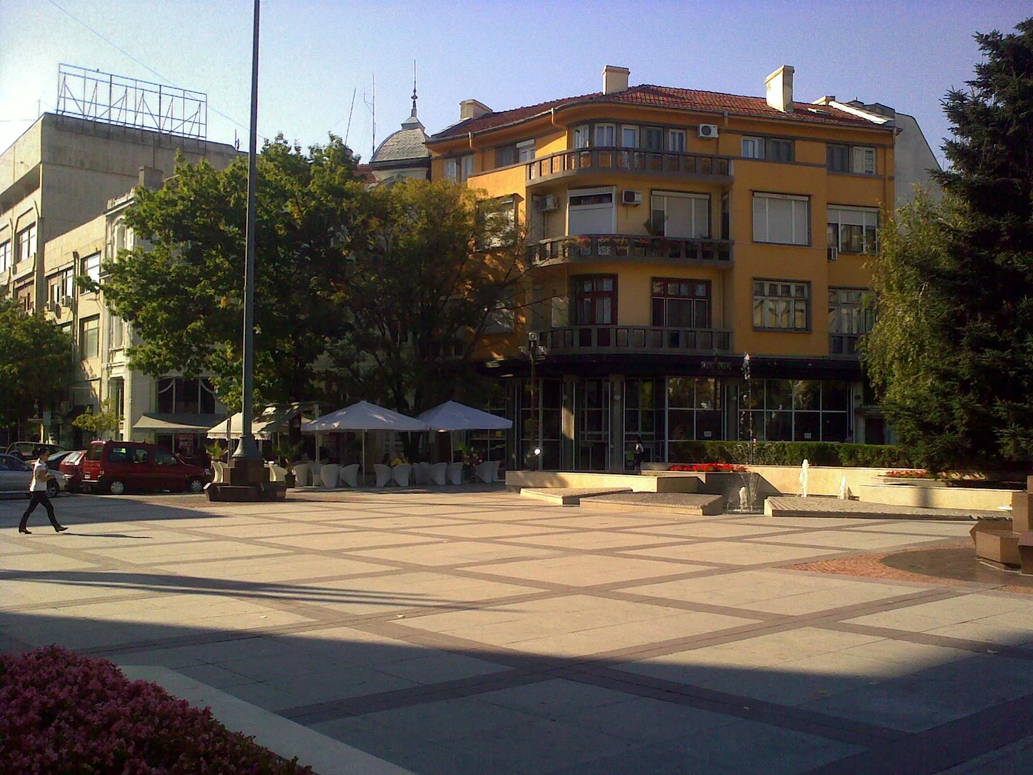 A paved square in central Burgas with cafe umbrellas and an ochre corner building