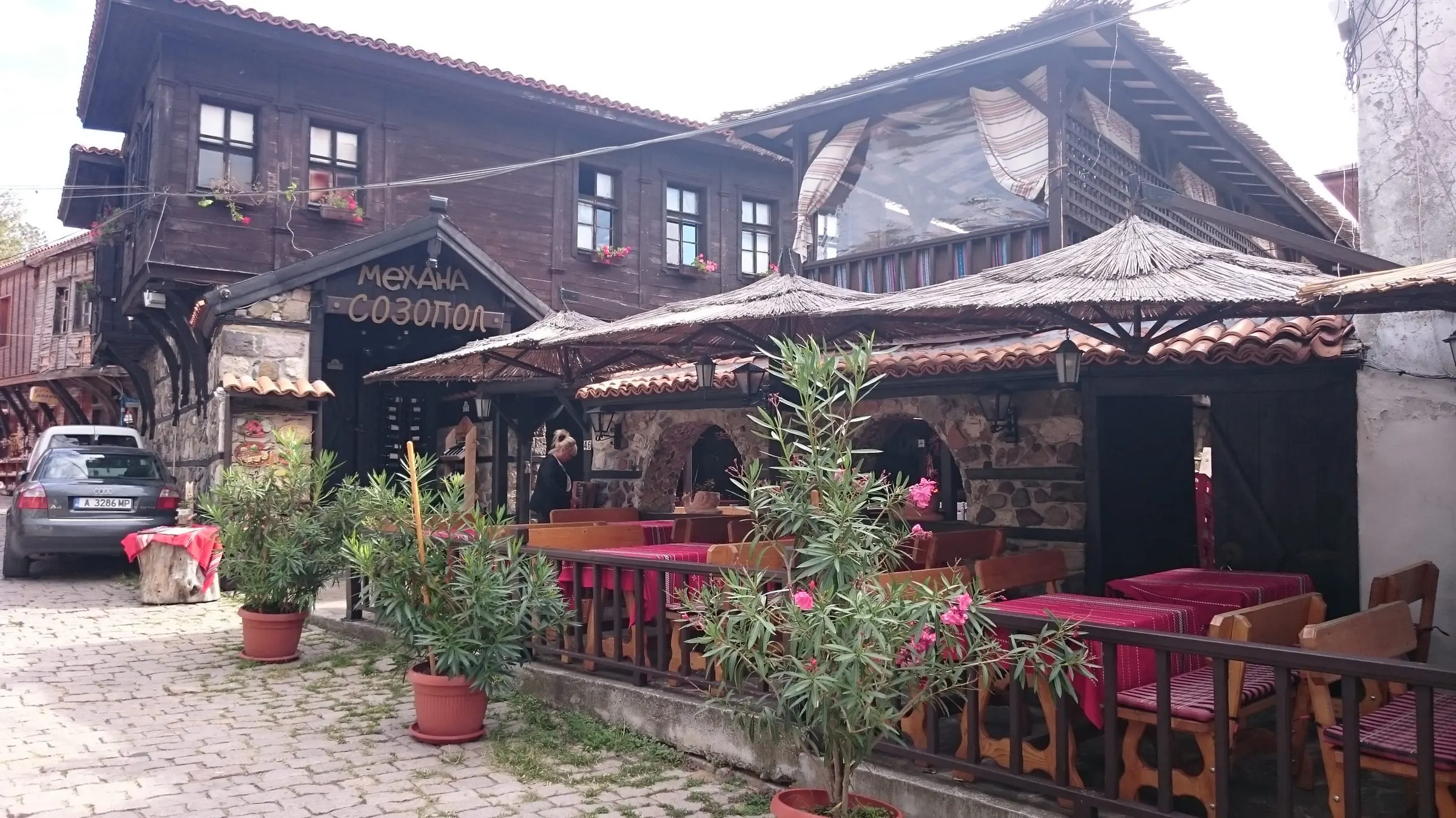 A taverna terrace under straw umbrellas beside a wooden house in Sozopol's old town