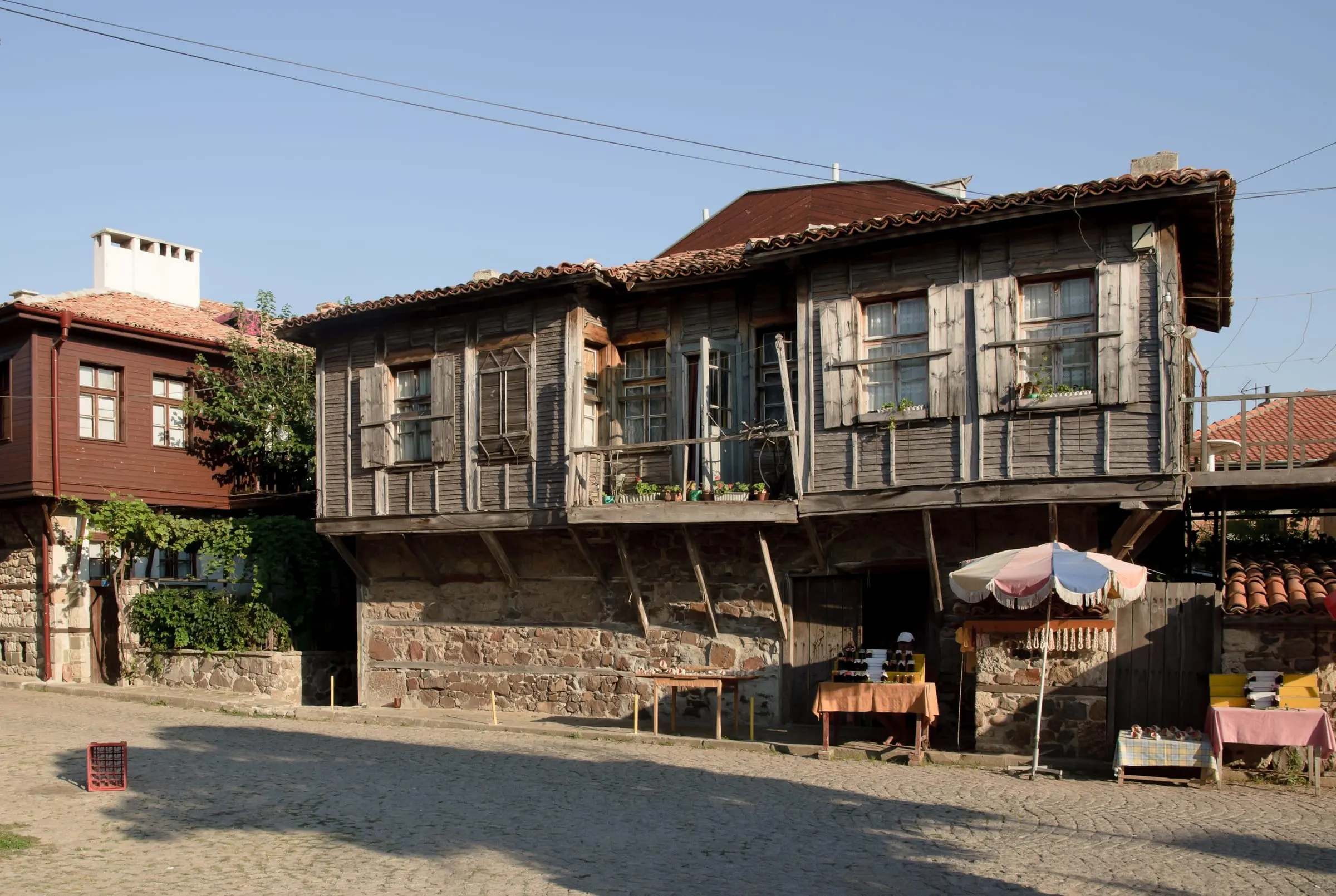 A timber house in Sozopol's old town at golden hour, with market stalls in front