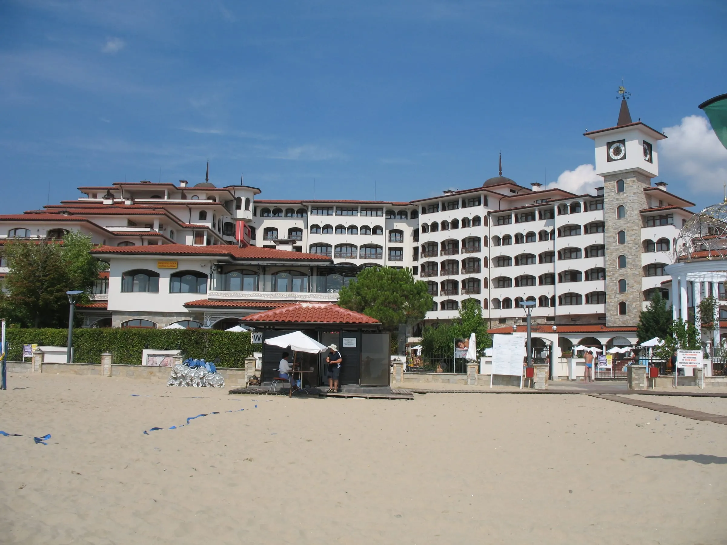 A large resort hotel complex with a clock tower directly behind the sand at Sunny Beach