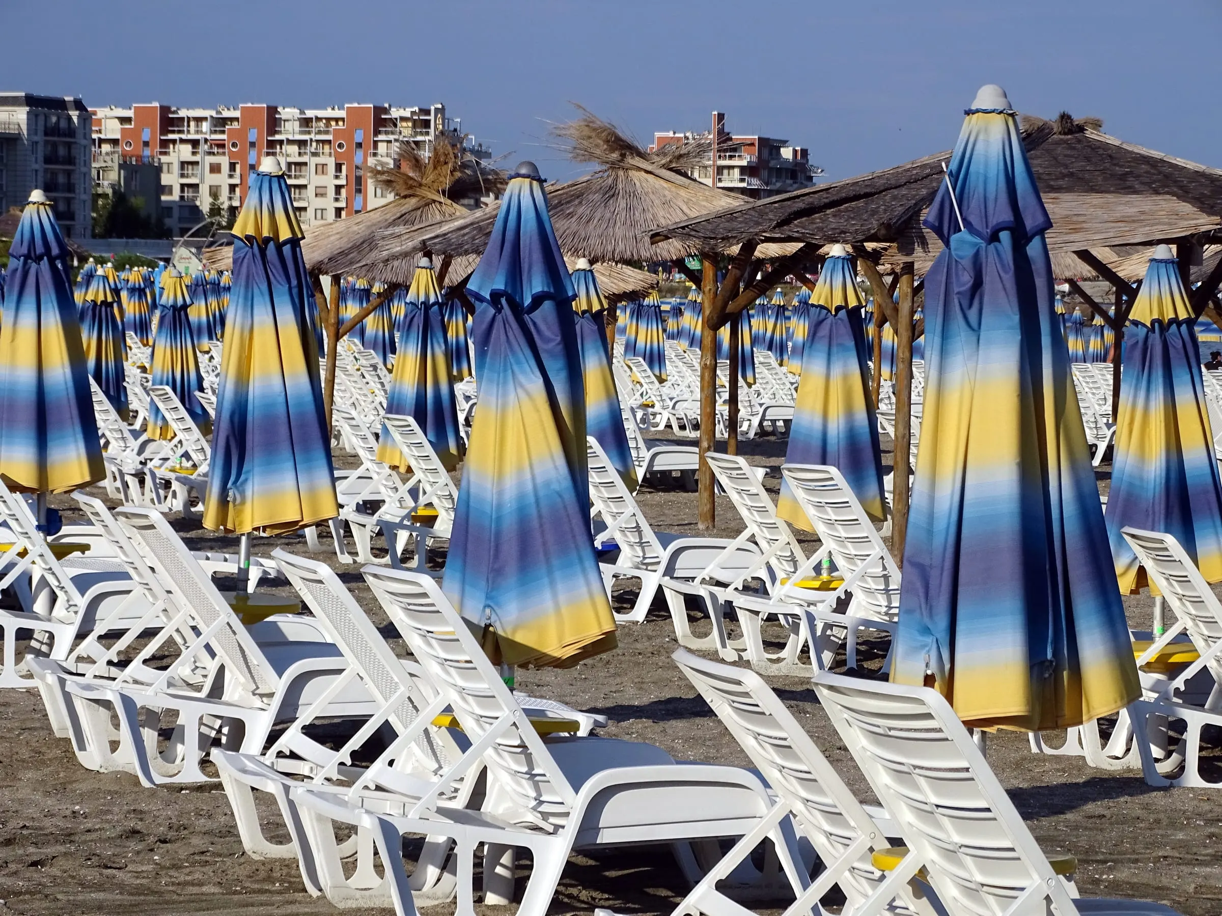 Rows of closed beach umbrellas and empty white sunbeds on the sand at Sunny Beach